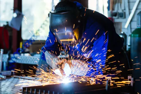 Schweißer mit Schutzmaske schweißt ein Metallbauteil, Funken sprühen