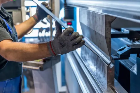 Fachkraft mit Arbeitshandschuhen legt ein Blech in eine Abkantpresse ein