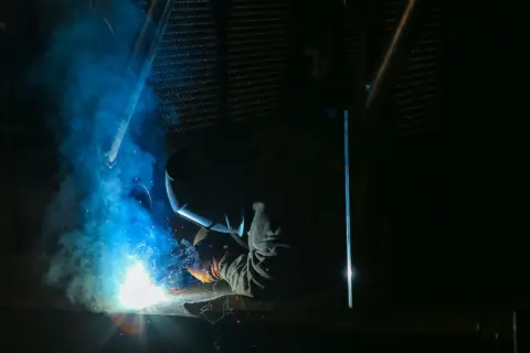 Schweißer bei der Arbeit, blaues Licht des Lichtbogens in einer dunklen Werkhalle